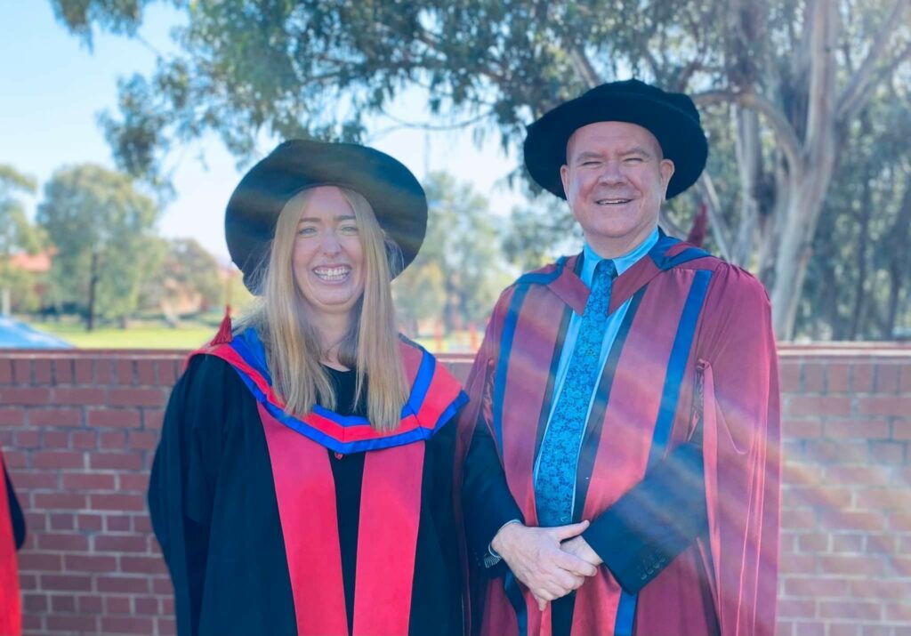 Dani Treweek and Andrew Cameron dressed in academic gowns smiling at the camera